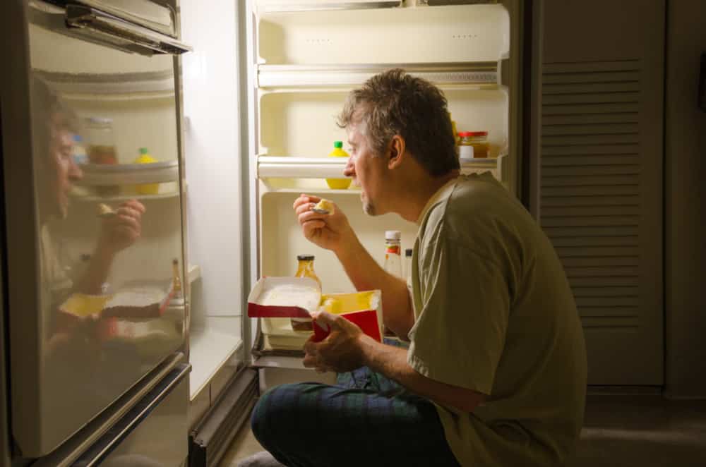 A man eats food out of the refrigerator.