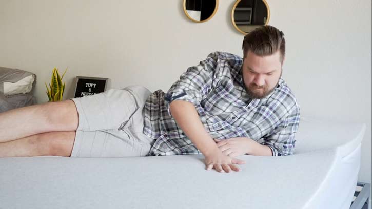 A man feels the cover of a mattress topper.