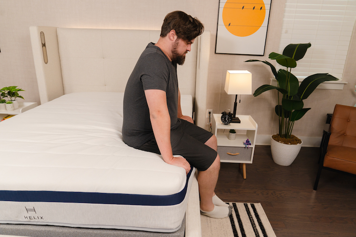 a man sits along the side of the Helix Midnight mattress