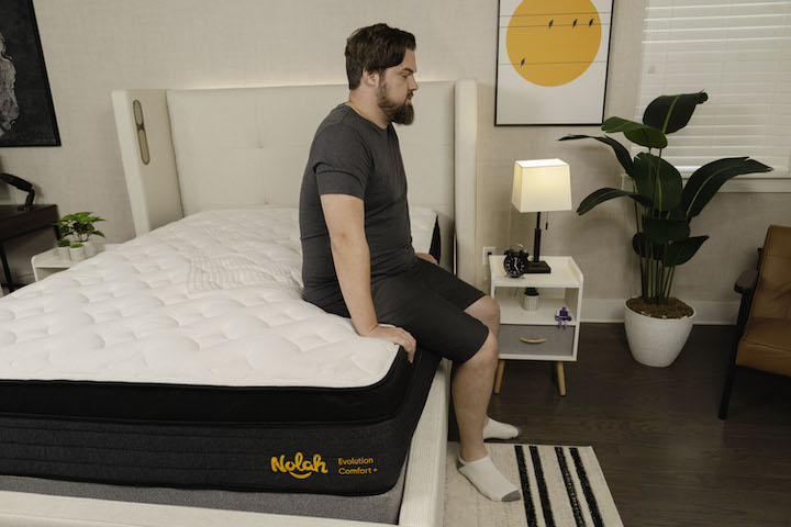a man sits on the edge of the Nolah Evolution Comfort + mattress