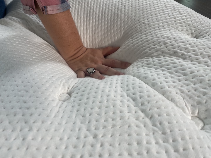a woman presses into the cover of the PlushBeds Signature Bliss mattress to see how it feels
