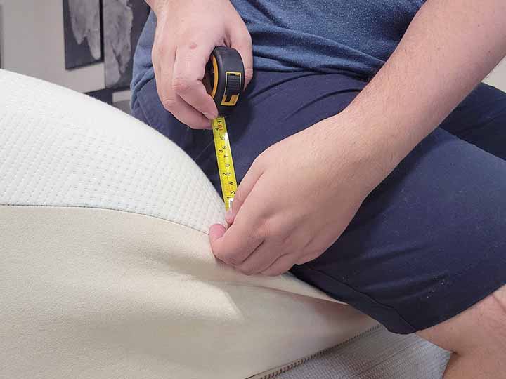 A close up image of a man holding a tape measure. The tape measure reads 3", as he shows how much sinkage is happening while sitting on the edge of the amttress.