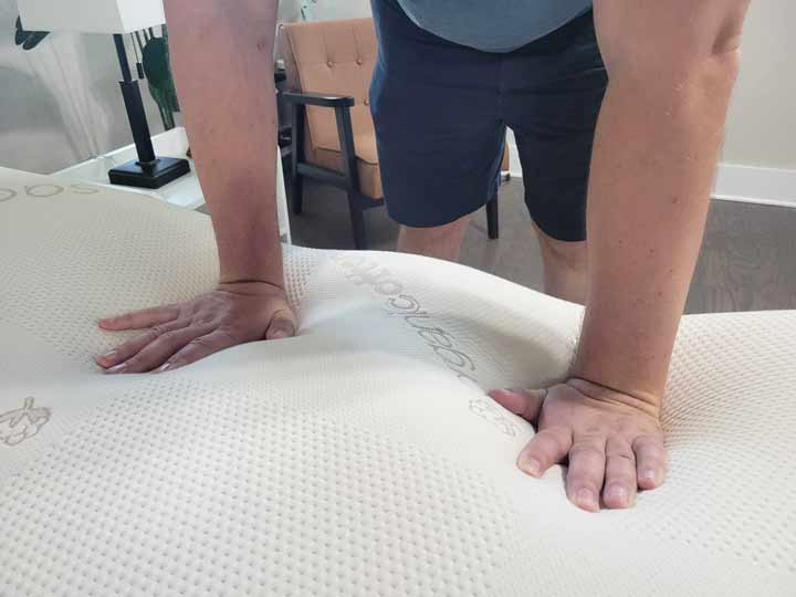 Two hands press into the top layers of the Saatva Contour5 mattress.