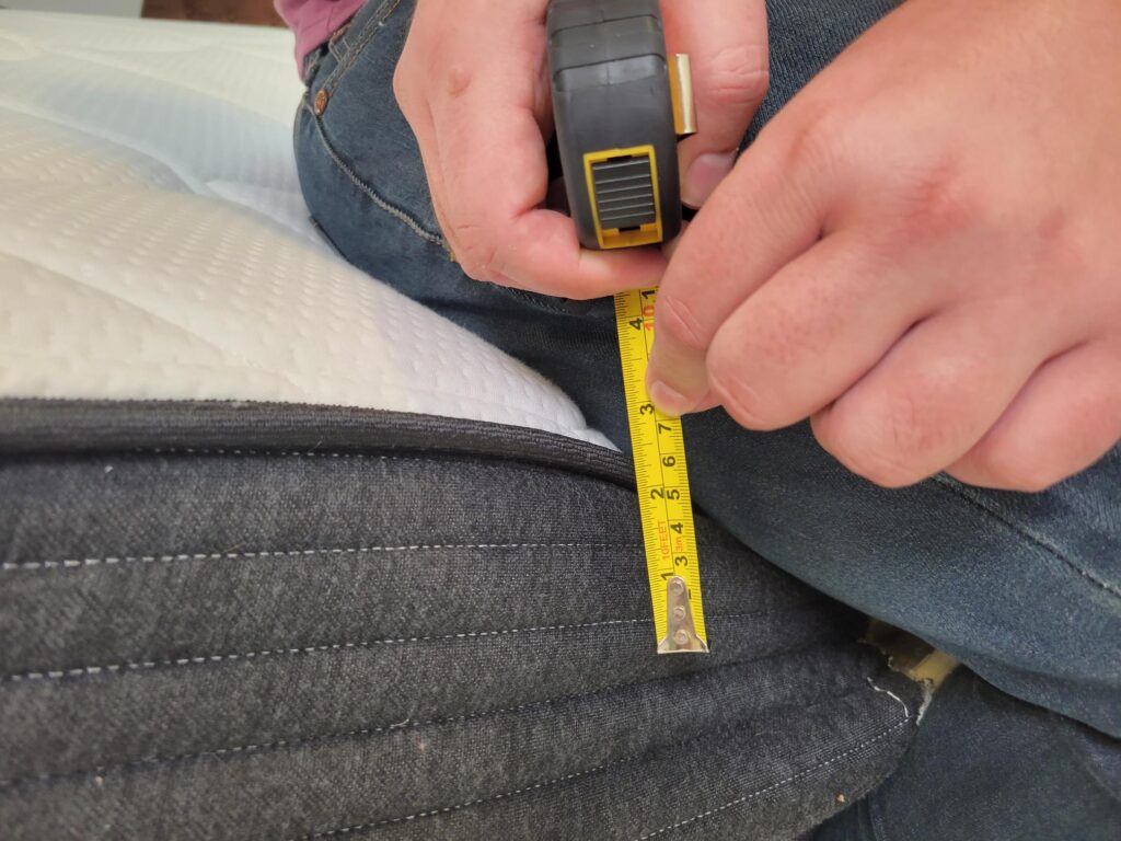 A man measuring how much the Plank mattress sinks when he sits on the edge of it