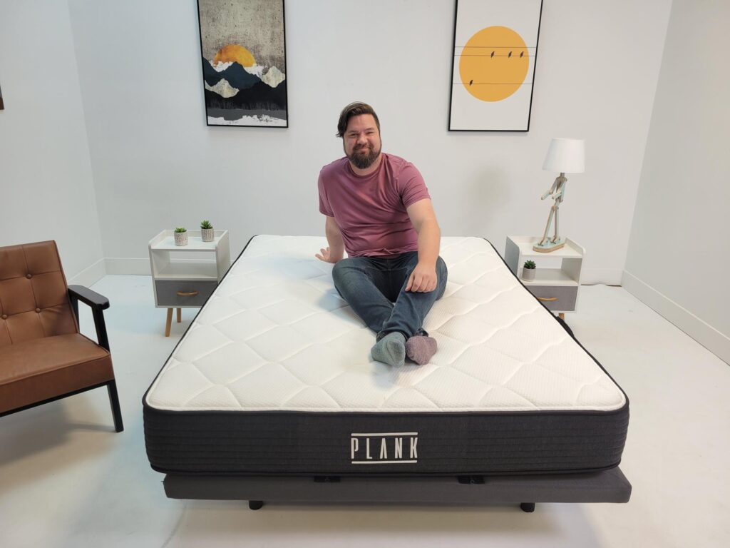 man sitting on Plank mattress smiling at camera