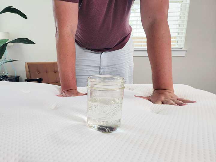 An image of a man pressing his hands into the top of the Brooklyn Bedding mattress. In front of him, there's a glass of water.