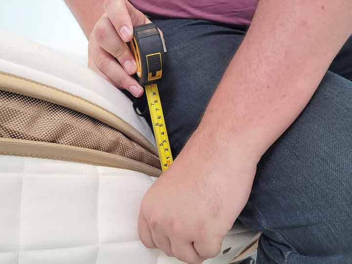 A close up image of a man using a tape measure to measure how much he compresses the side of the Cloverlane Hybrid Mattress.