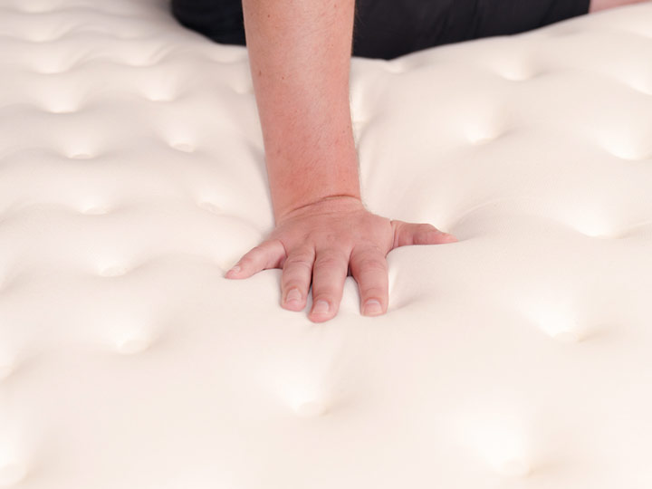 An image of a single hand pressing into the Cloverlane Hybrid mattress.