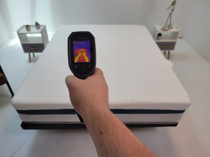 A temperature gun is pointed at the surface of the Helix Twilight mattress, displaying the thermal outline of a man with a temperature of 77.7 degrees Fahrenheit