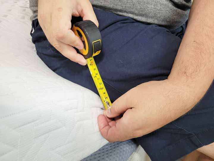 A close up image of Marten holding the tape measure to show how much the Nectar Premier Mattress sinks when sitting on the edge.