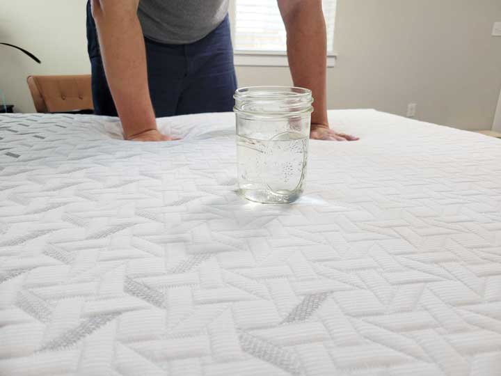 An image showing Marten press his hands into the top of the Nectar Premier mattress, with a glass of water in front of him.