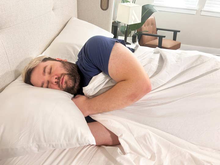 An image of a man sleeping on his side while using the Peacock Alley Soprano Sateen shees.