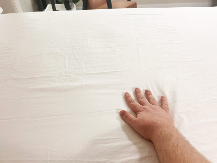 An image of a hand brushing over the white Peacock Alley Soprano Sateen Sheets.